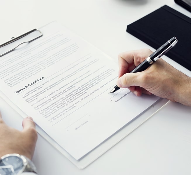 A pair of hands using a pen to sign a terms & conditions document